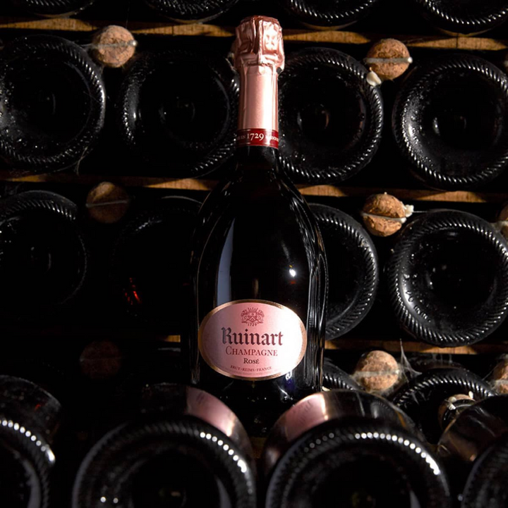 Bottle of Ruinart Rosé Champagne elegantly displayed in a traditional wine cellar surrounded by stacked bottles.