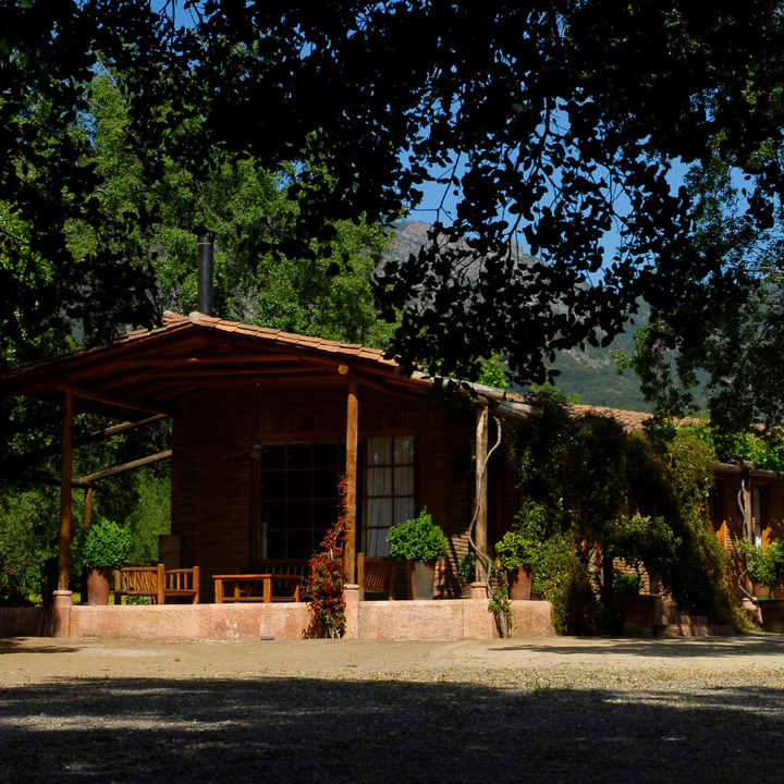 A rustic winery house nestled in a Chilean vineyard surrounded by lush trees and mountains, creating a tranquil countryside setting.