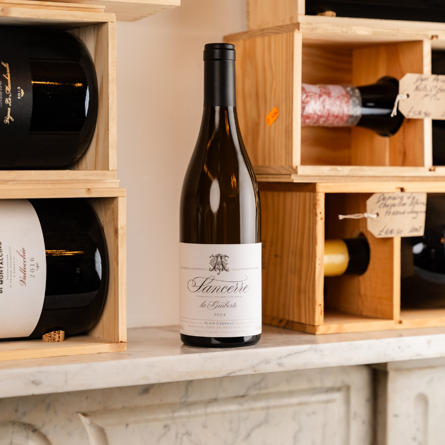 A bottle of Sancerre La Giberte 2023 by Alain Gueneau displayed on a marble shelf, surrounded by wooden wine crates with other fine wines and gourmet products, highlighting a sophisticated wine selection.