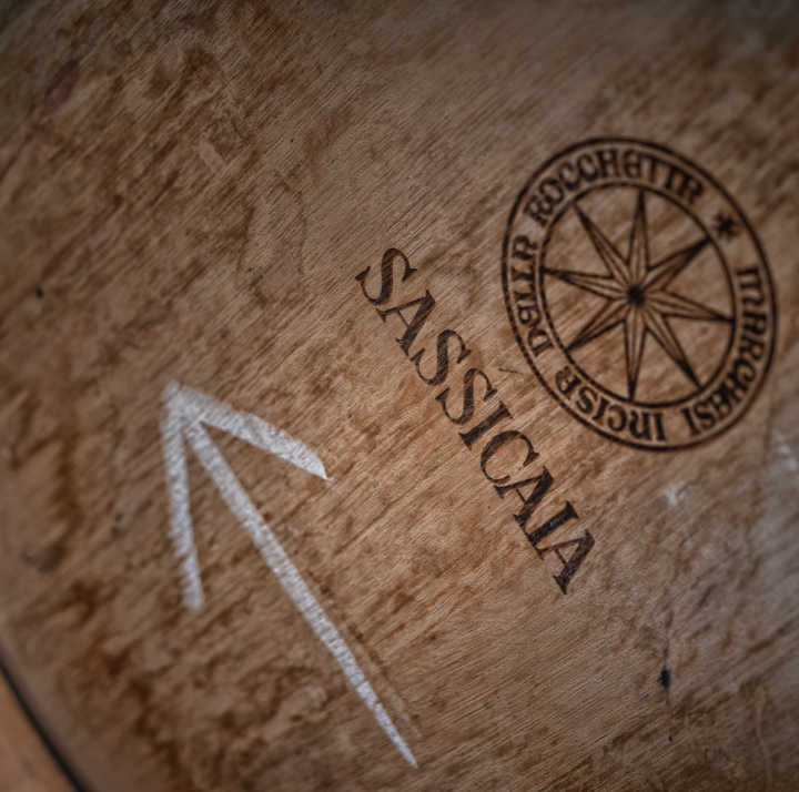 A close-up of a wooden wine barrel stamped with the Sassicaia logo, showcasing the craftsmanship of winemaking.