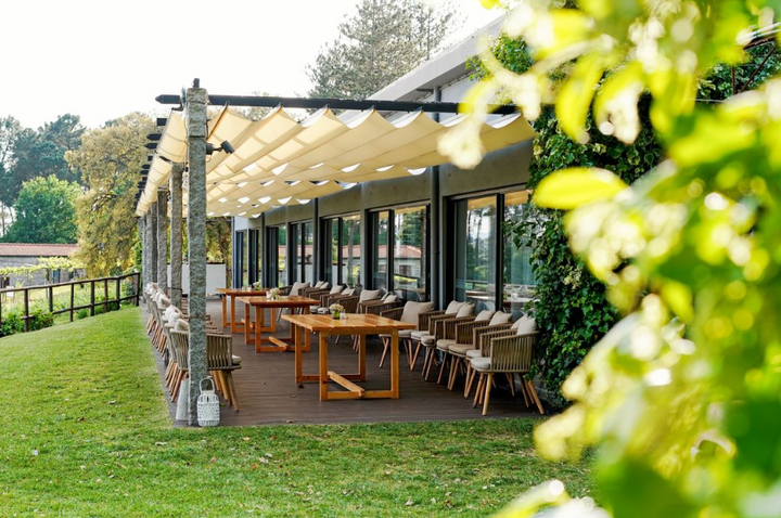 A beautifully arranged outdoor terrace at Solar das Bouças estate with wooden tables and chairs, surrounded by lush greenery and sunshine.