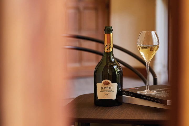 A bottle of Taittinger Comtes de Champagne Blanc de Blancs with a glass of Champagne on a table, capturing an elegant and refined ambiance.