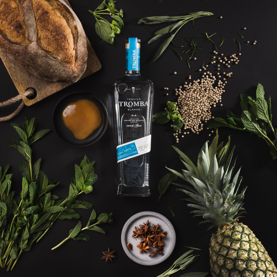 Tequila Tromba Blanco bottle surrounded by fresh ingredients like mint, pineapple, and herbs, highlighting its natural flavour profile.