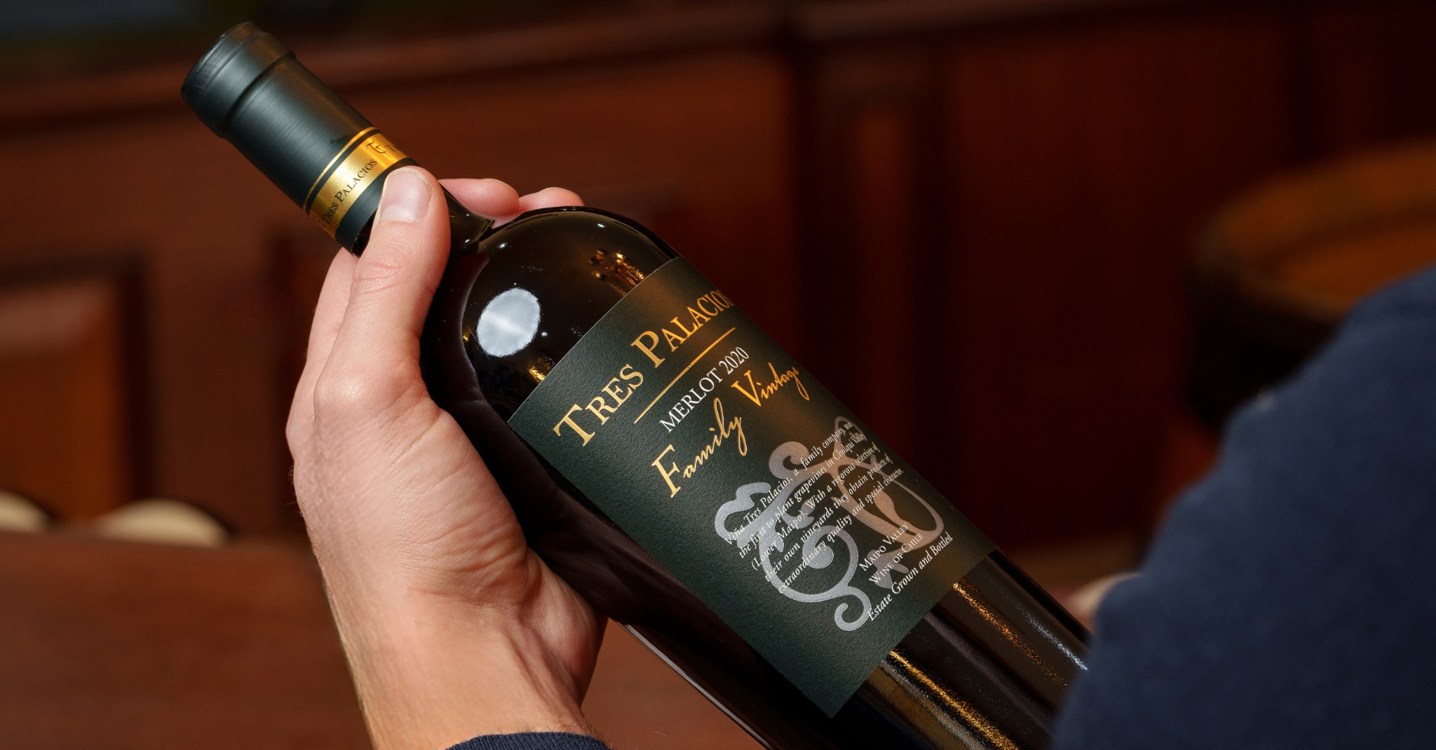 Close-up of a bottle of Tres Palacios 2020 Merlot Family Vintage held by a person, showcasing the elegant green label with gold accents.