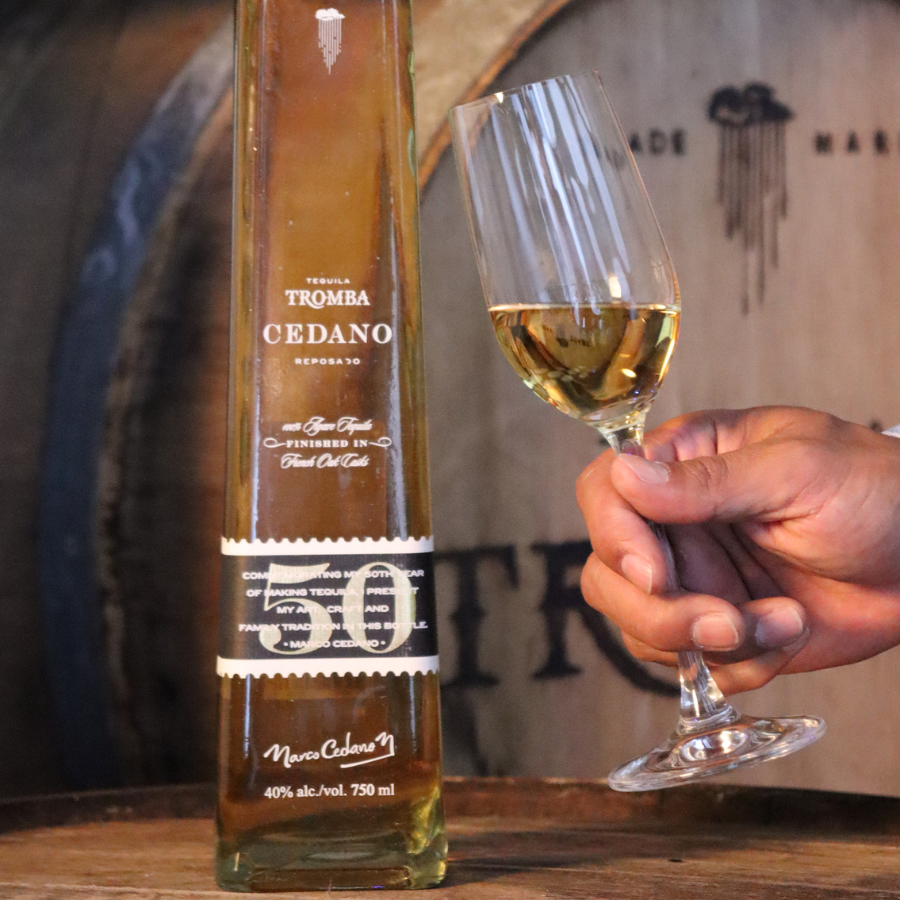 A glass of Tromba Cedano Reposado Tequila alongside its bottle, emphasizing the golden hue of the premium tequila.