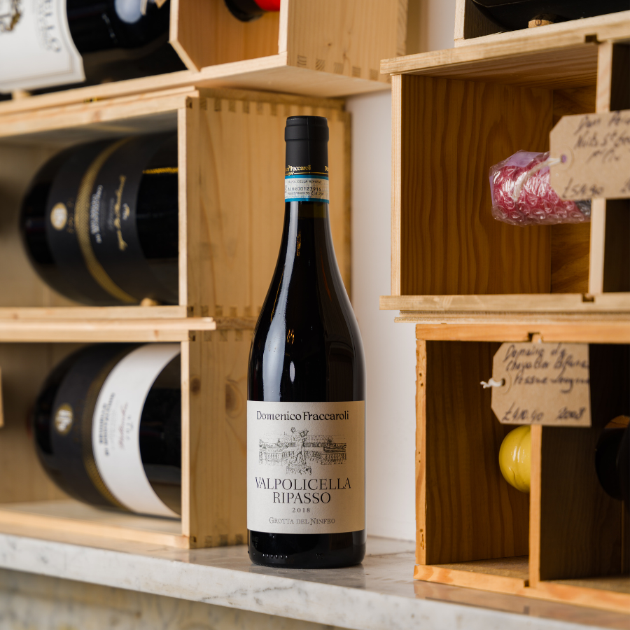 A bottle of Domenico Fraccaroli Valpolicella Ripasso 2018 wine displayed on a marble countertop, surrounded by wooden shelves with other wines and delicacies, creating a rustic and premium ambiance.