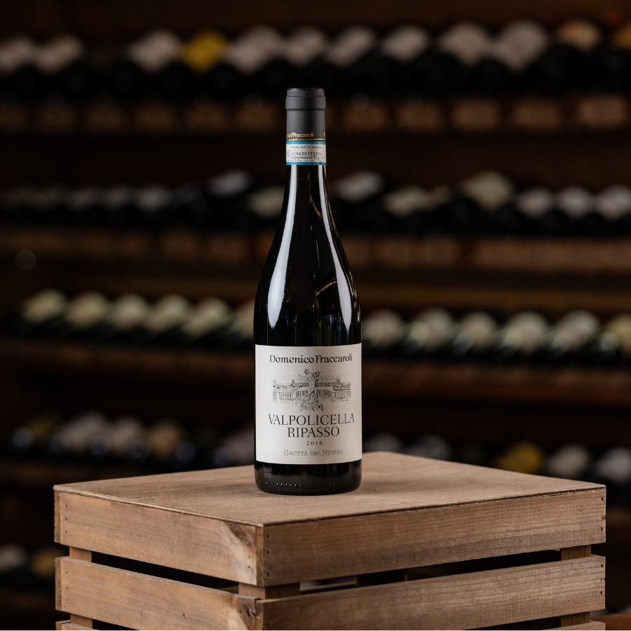 A bottle of Valpolicella Ripasso by Domenico Fraccaroli, an Italian red wine, resting on a wooden crate in front of a wine cellar.