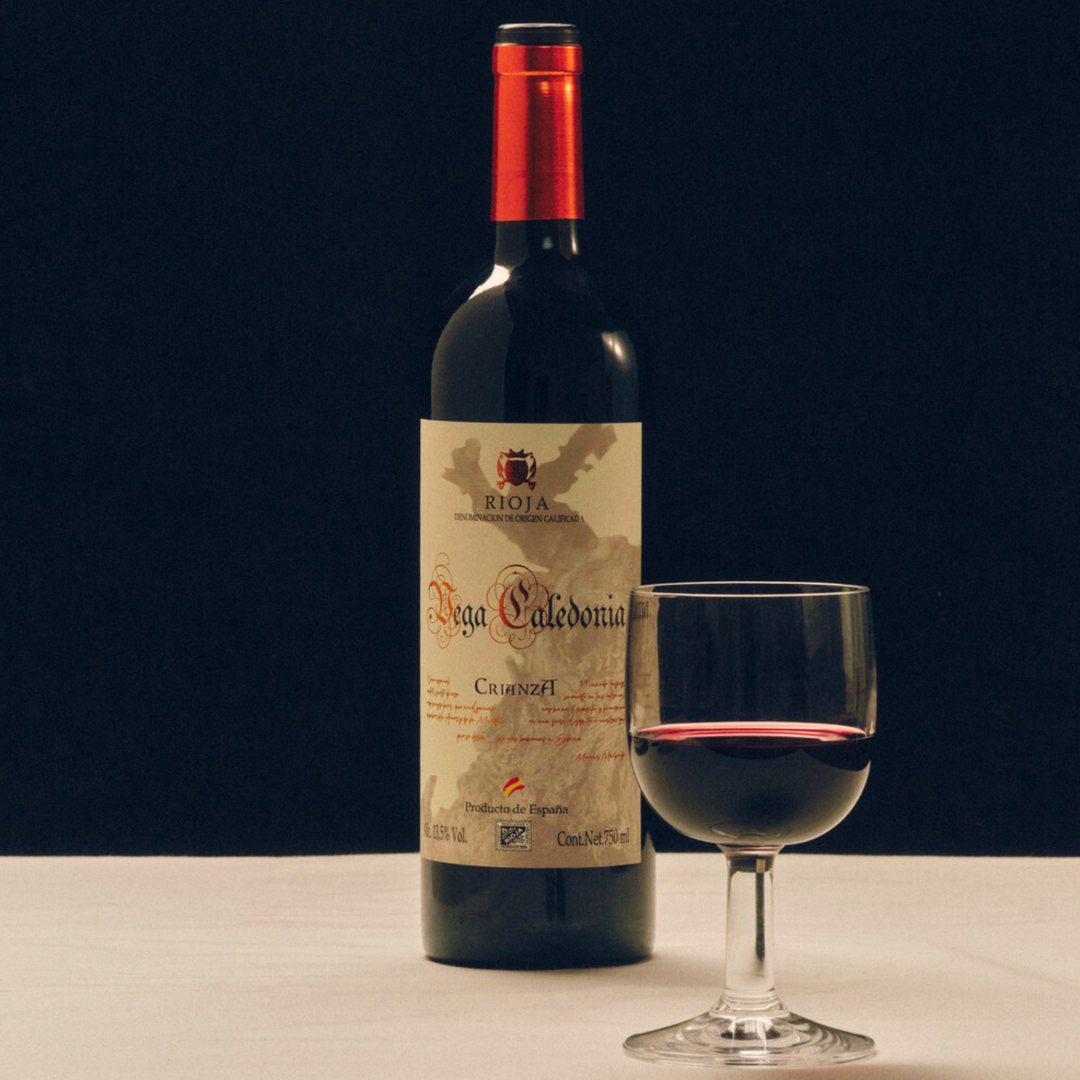 Vega Caledonia Rioja Crianza red wine bottle with a glass of red wine, set against a dark background for an elegant presentation.