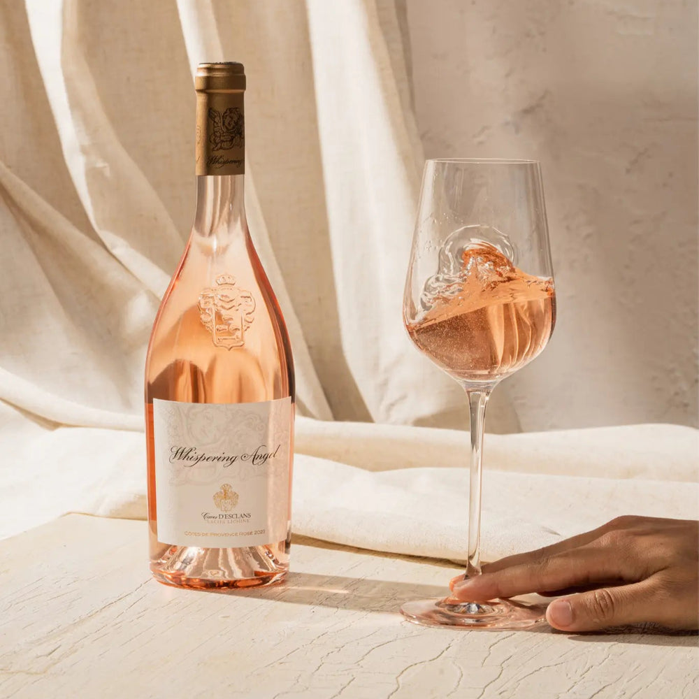 Whispering Angel Rosé wine bottle with a glass of rosé on a white textured table, elegantly staged with soft lighting.