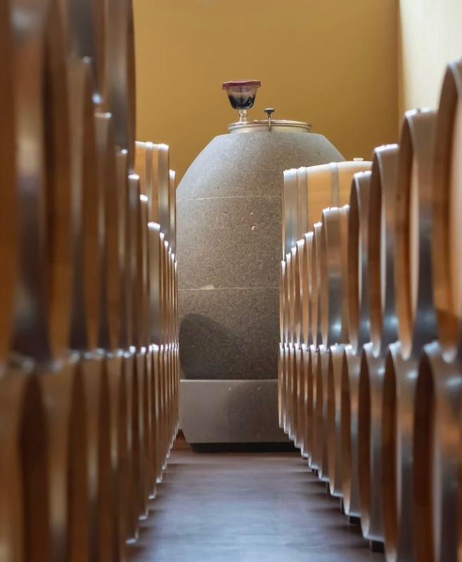 A modern wine cellar featuring a concrete egg fermentation tank surrounded by wooden barrels, showcasing innovative winemaking techniques.