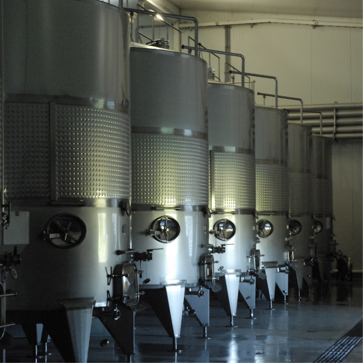 A row of stainless steel fermentation tanks inside a wine production facility, showcasing modern winemaking processes.