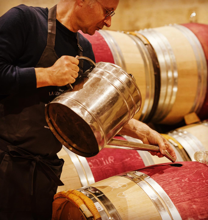 A winemaker carefully tending to a wine barrel in La Conseillante wine cellar, showcasing traditional winemaking craftsmanship.